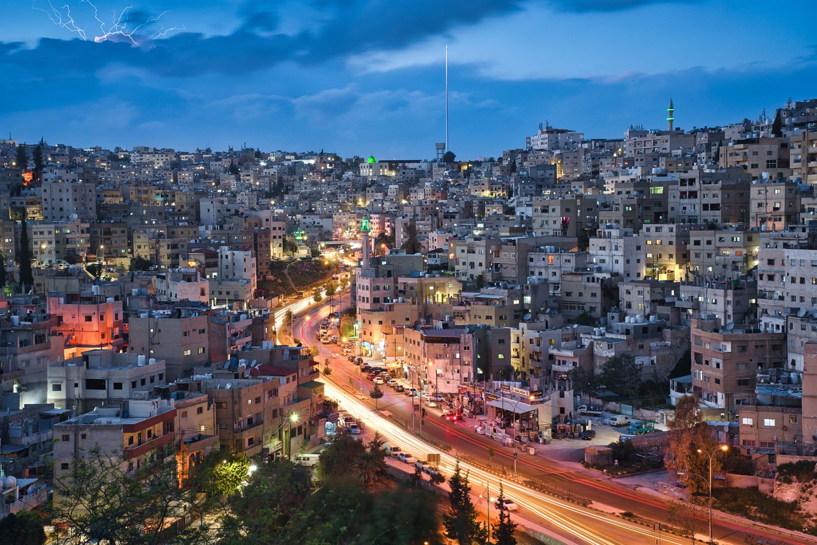 Hillside houses of Amman glowing at sunset with traffic lights streaking through the valley, Jordan