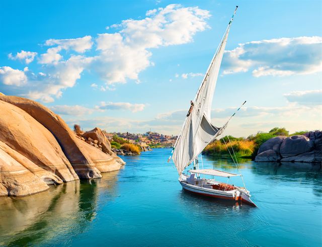 Felucca sailing past smooth granite boulders on the blue Nile at Aswan