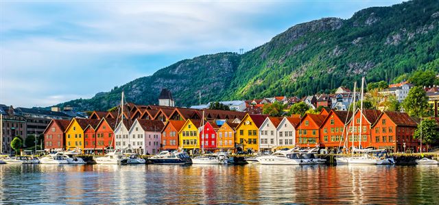 Colorful Hanseatic wharf houses of Bryggen in Bergen reflected in the harbor below green hills