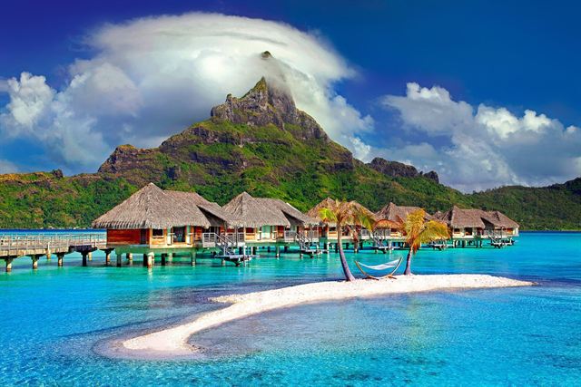 Mount Otemanu on Bora Bora rising behind overwater bungalows and a white sandbar lagoon
