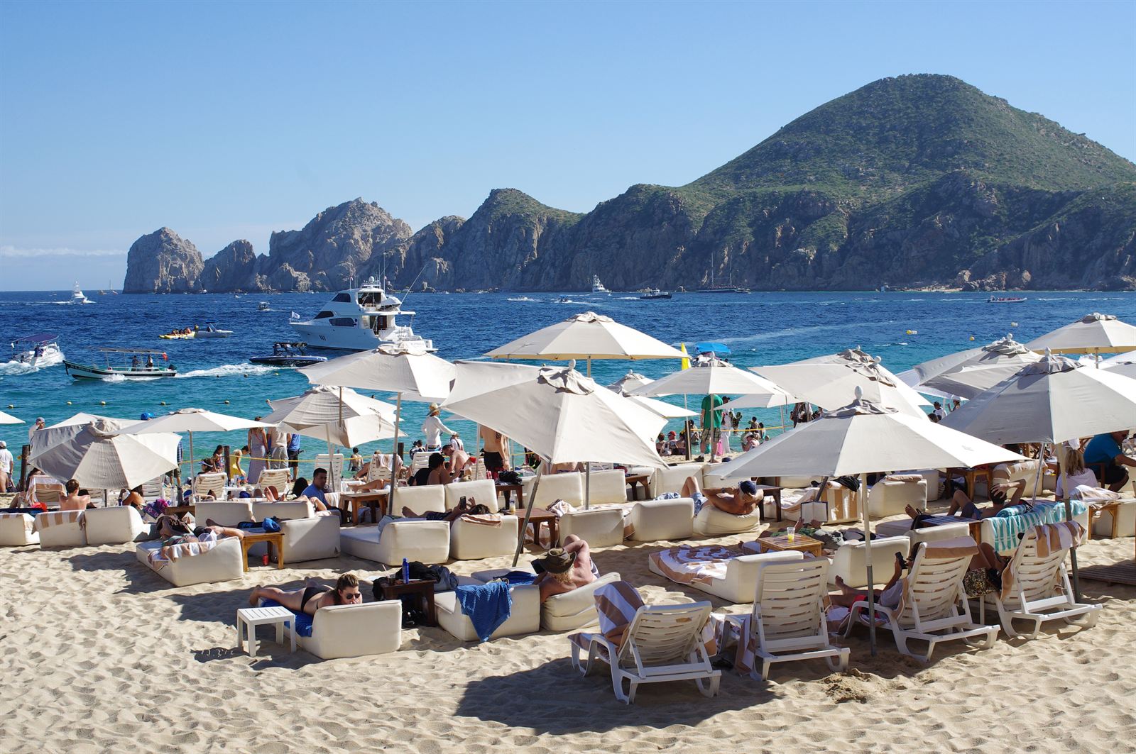 Crowded Medano Beach umbrellas and boats with the Land's End rock arch headland beyond, Cabo San Lucas