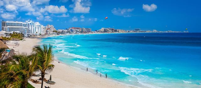 Cancun beach with palms, white sand and hotels along bright turquoise Caribbean water