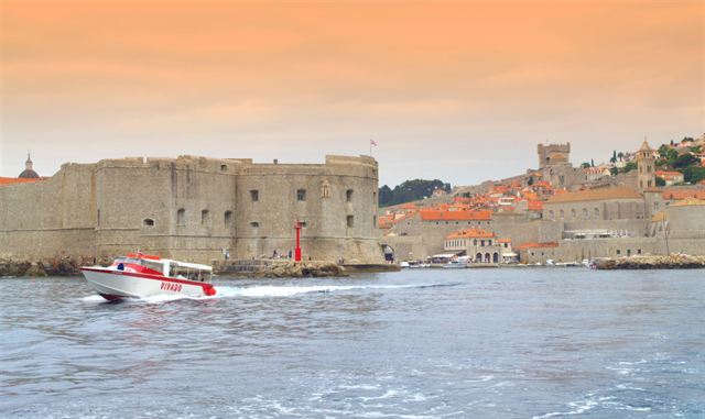 Stone city walls and fortress of Dubrovnik Old Town seen from the sea with a speedboat