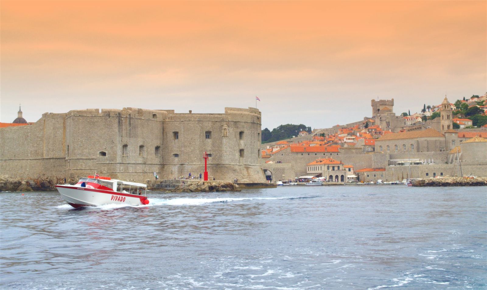 Stone city walls and fortress of Dubrovnik Old Town seen from the sea with a speedboat