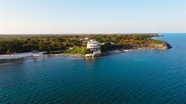 Aerial view of a white beachfront estate on a green point above deep blue water on the Grand Cayman coast