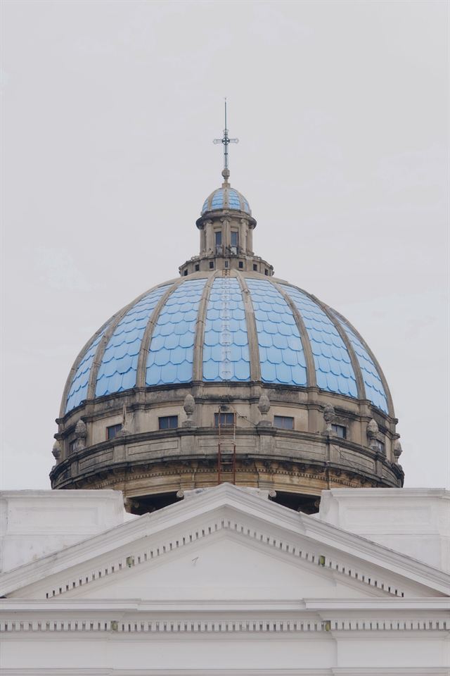 Blue-tiled dome and lantern of the Metropolitan Cathedral in Guatemala City against a pale sky