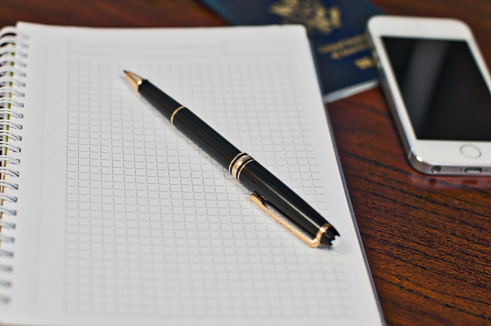 Open notebook with a fountain pen, a smartphone and a passport on a wooden desk