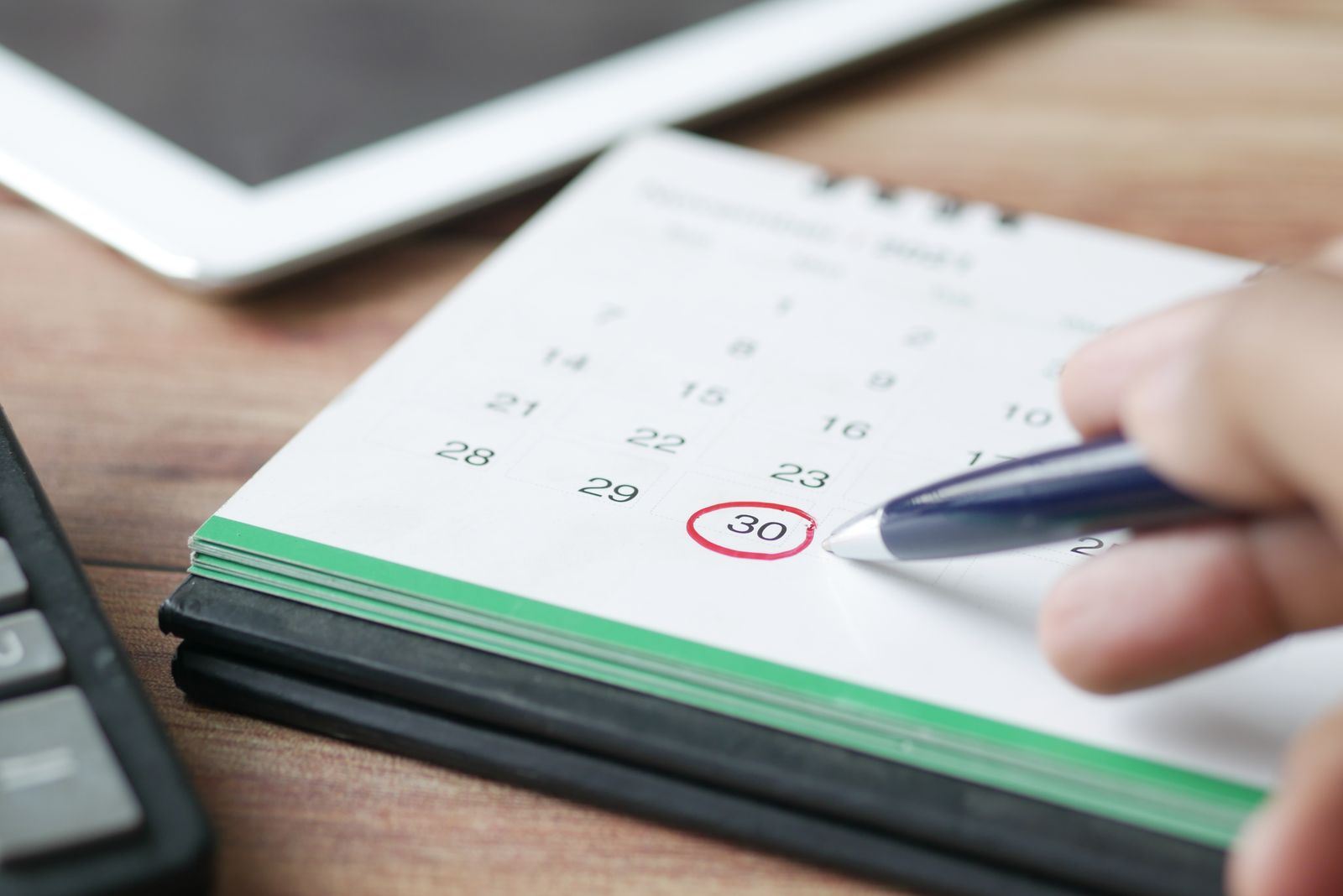 Hand circling a date on a desk calendar with a pen