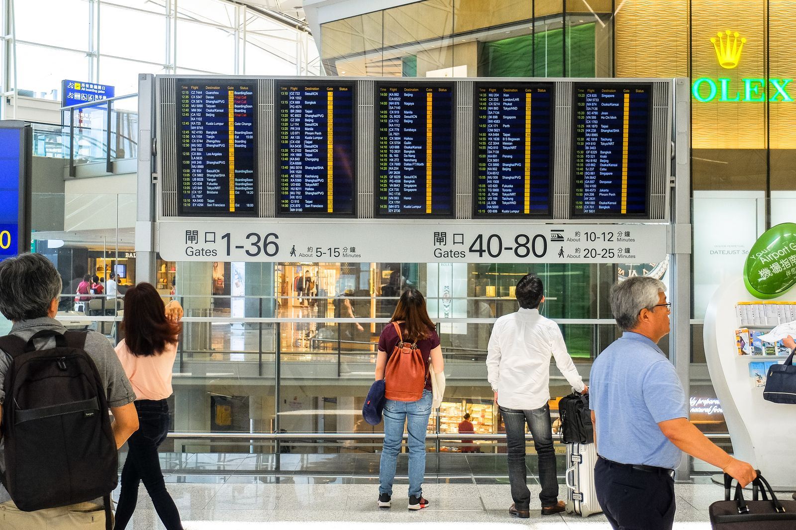 Travelers with luggage reading departure boards and gate signs in a large international airport terminal
