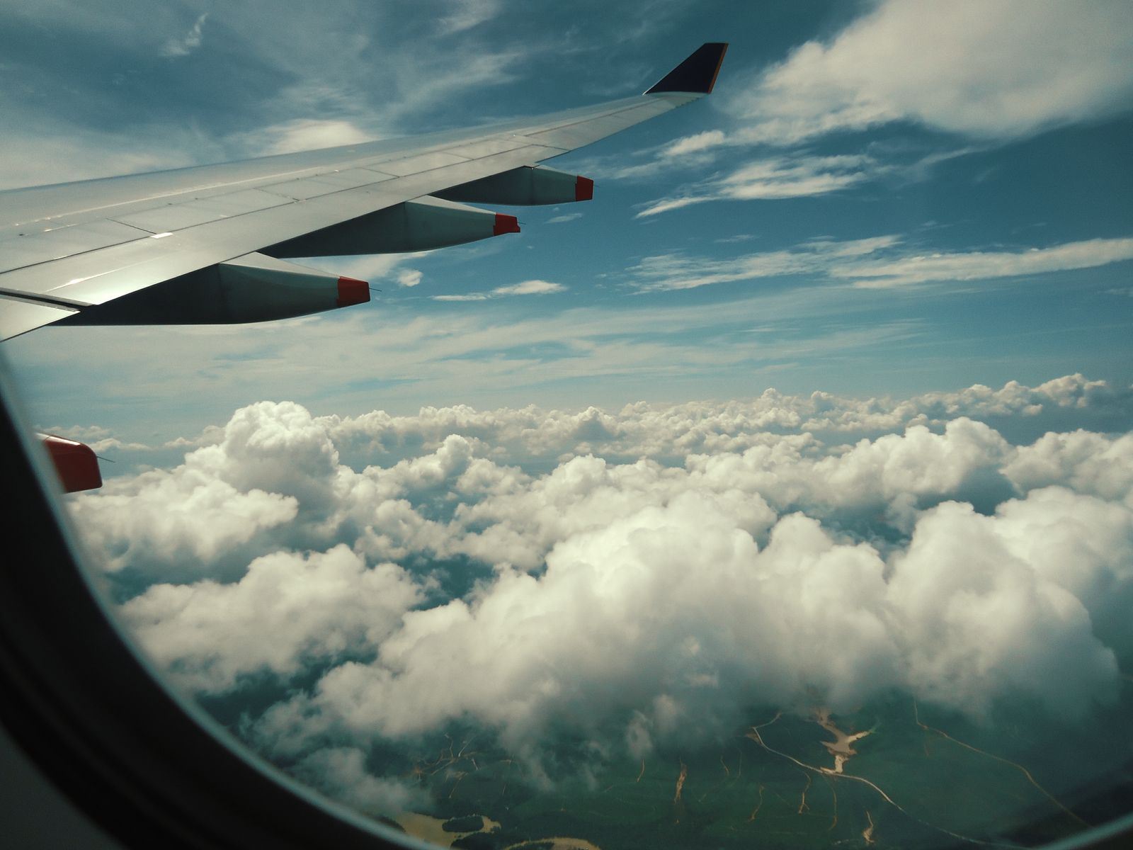 Airliner wing above a sea of white clouds seen through a cabin window