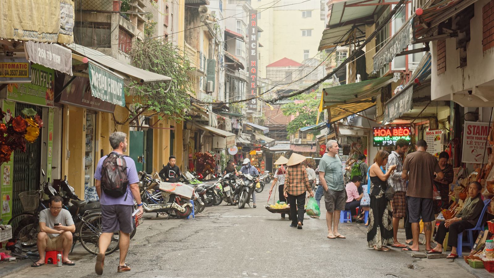 Street in Hanoi's Old Quarter with shop houses, pedestrians and parked motorbikes, Vietnam