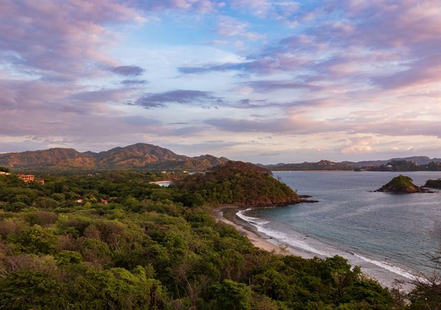 Forested Guanacaste coastline and sandy bay on the Papagayo Peninsula under a pink sunset sky