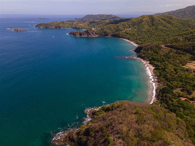 Aerial view of a curving turquoise bay and dry tropical forest hills on Costa Rica's Guanacaste coast