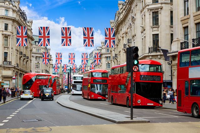 Red double-decker buses on a London street hung with Union Jack flags