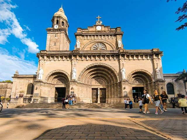 Manila Cathedral's Romanesque Revival facade and bell tower in Intramuros under bright blue sky