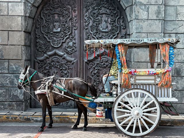 Decorated calesa horse carriage in front of carved stone church doors in Intramuros, Manila