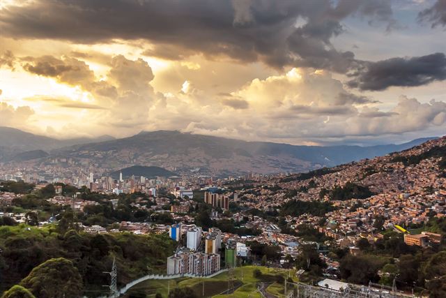 Medellin skyline and hillside neighborhoods in the Aburra Valley beneath golden sunset clouds