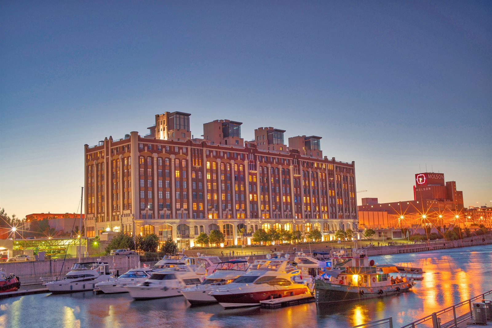 Yachts in the Old Port marina below a lit brick warehouse building, with the Molson brewery sign beyond, Montreal