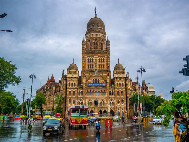 Gothic BMC municipal headquarters building in Mumbai with traffic and a red bus in the rain