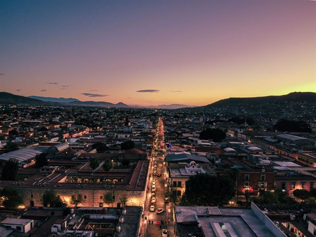 Oaxaca City at sunset with a lit avenue running toward the surrounding mountains under a violet sky