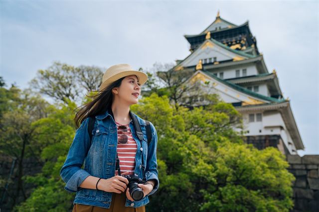 Traveler with a camera in front of the white and green Osaka Castle keep