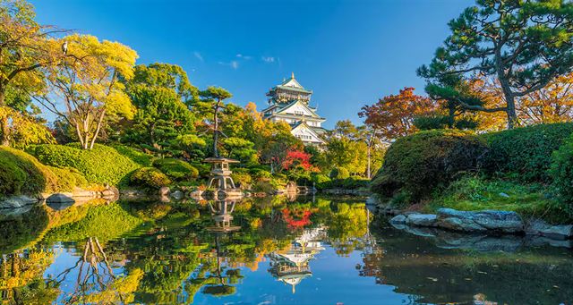 Osaka Castle rising above autumn trees reflected in a garden pond