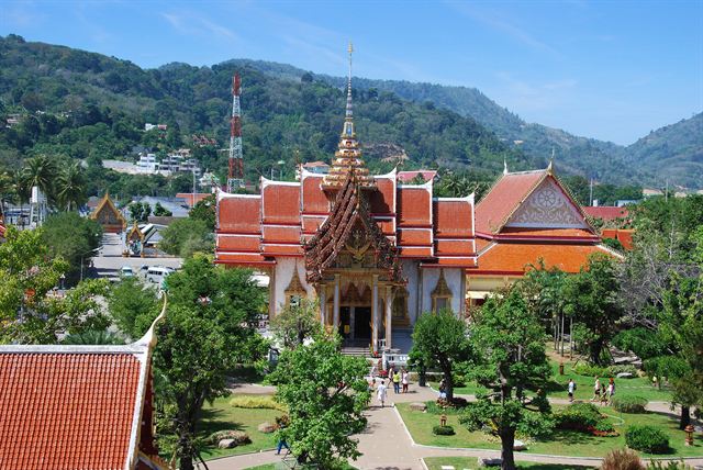 Red and gold roofs of Wat Chalong temple among gardens and hills in Phuket, Thailand