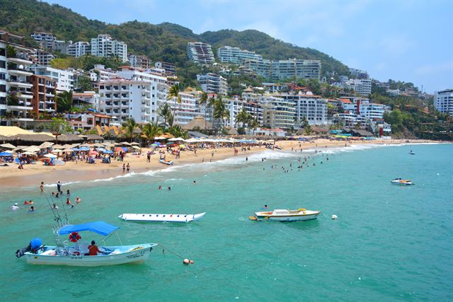 Turquoise water, boats and a busy beach below hillside hotels in Puerto Vallarta, Mexico