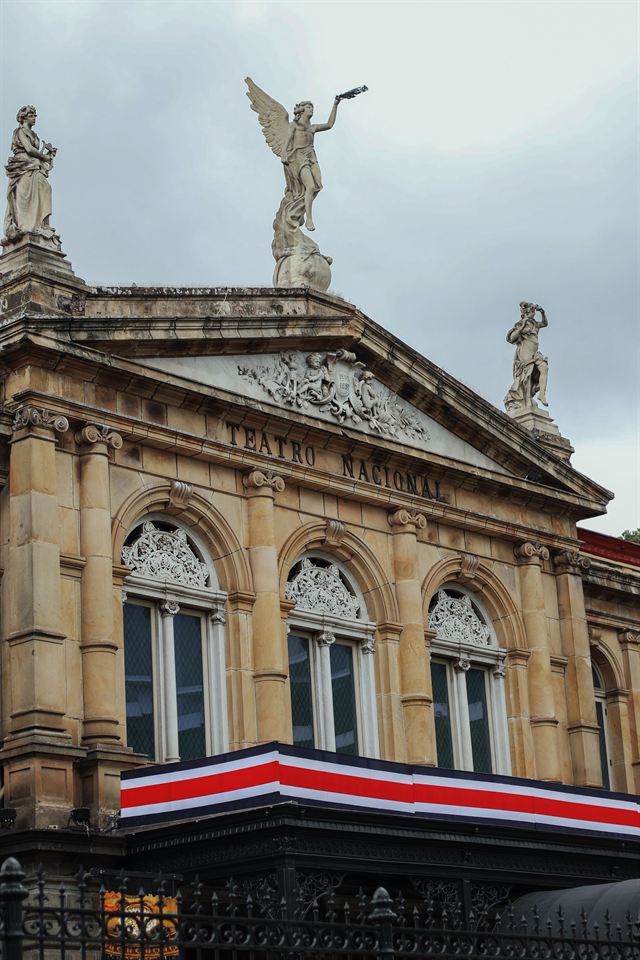 Ornate neoclassical facade and statues of the Teatro Nacional de Costa Rica in San Jose with a Costa Rican flag