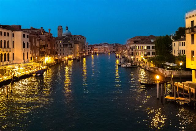 Grand Canal in Venice lined with colorful palazzi, vaporetto stops, gondolas and water taxis under blue sky